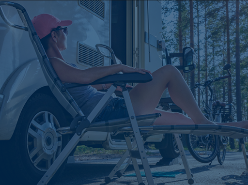 woman relaxing in a folding chair next to an RV parked in the woods
